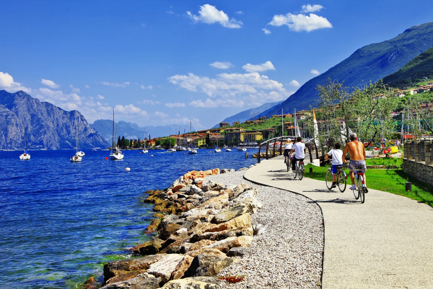 A curved path next to lake, with several people on bicycles; mountains in distance