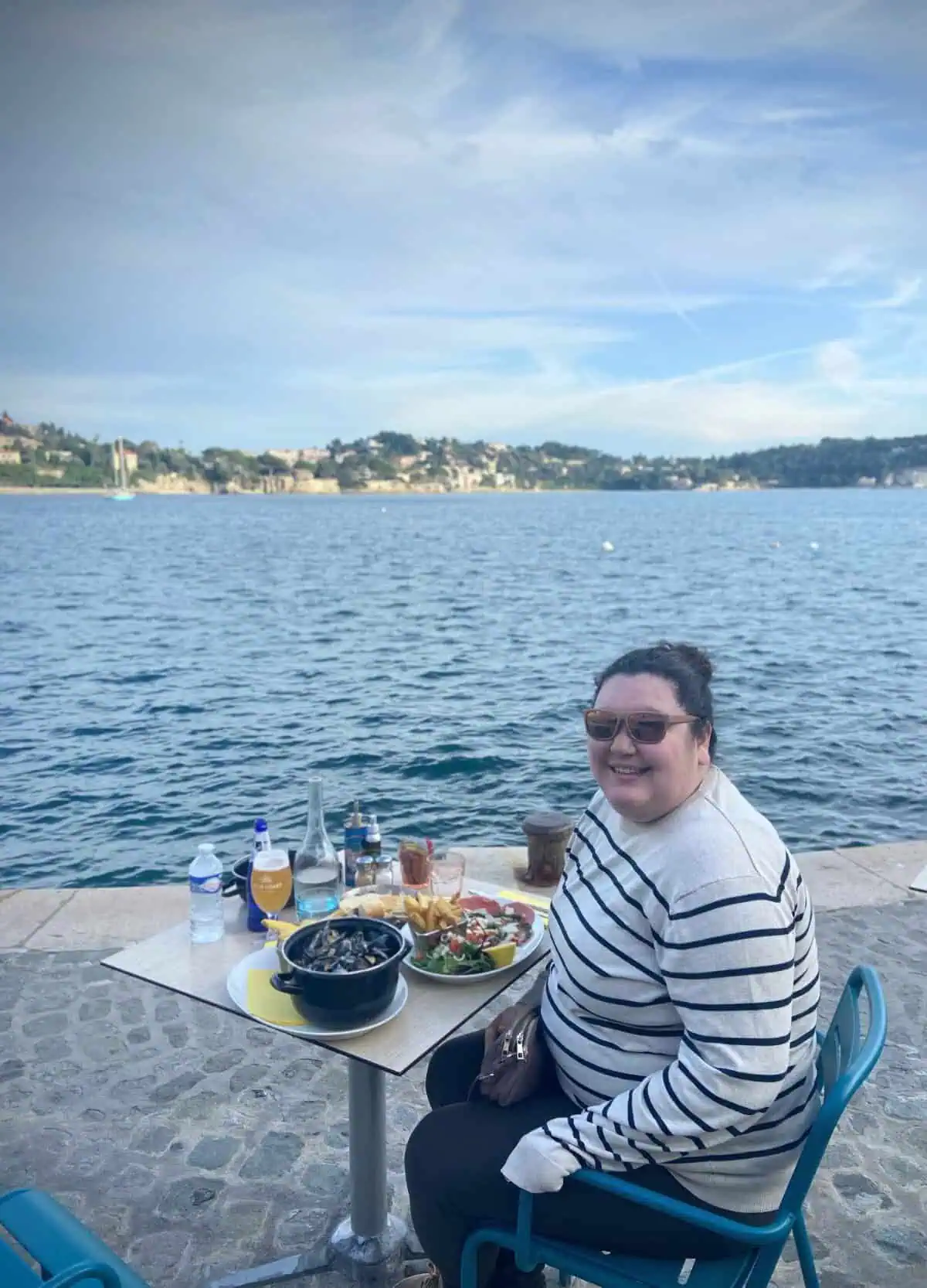 Riana sitting by the water in Villefranche sur Mer with a table full of mussels and beef carpaccio