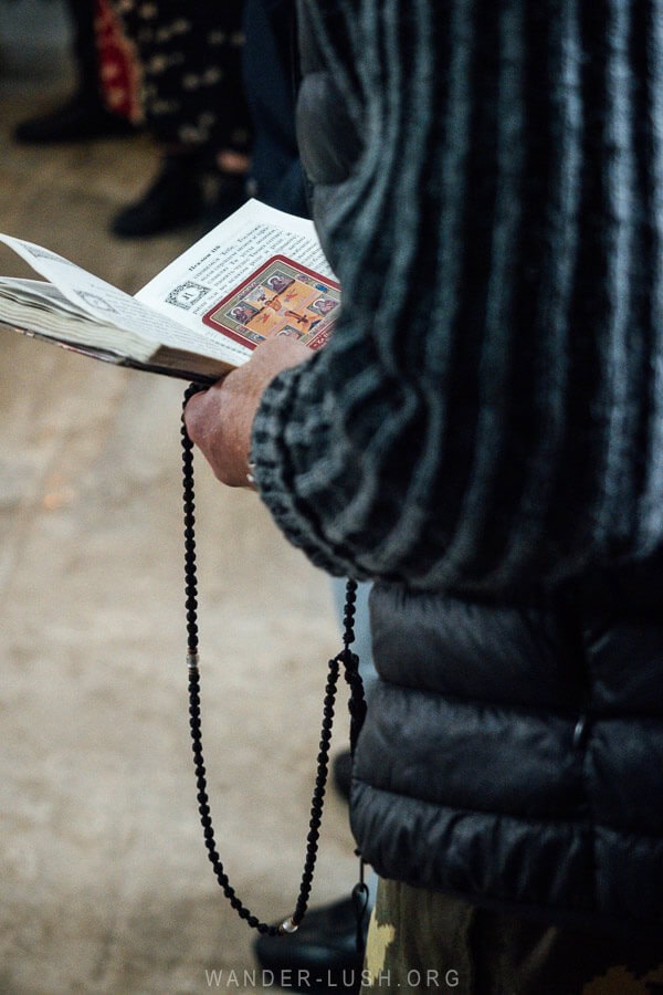 A man clasps a prayer book and a long set of beads during Orthodox liturgy in Georgia.