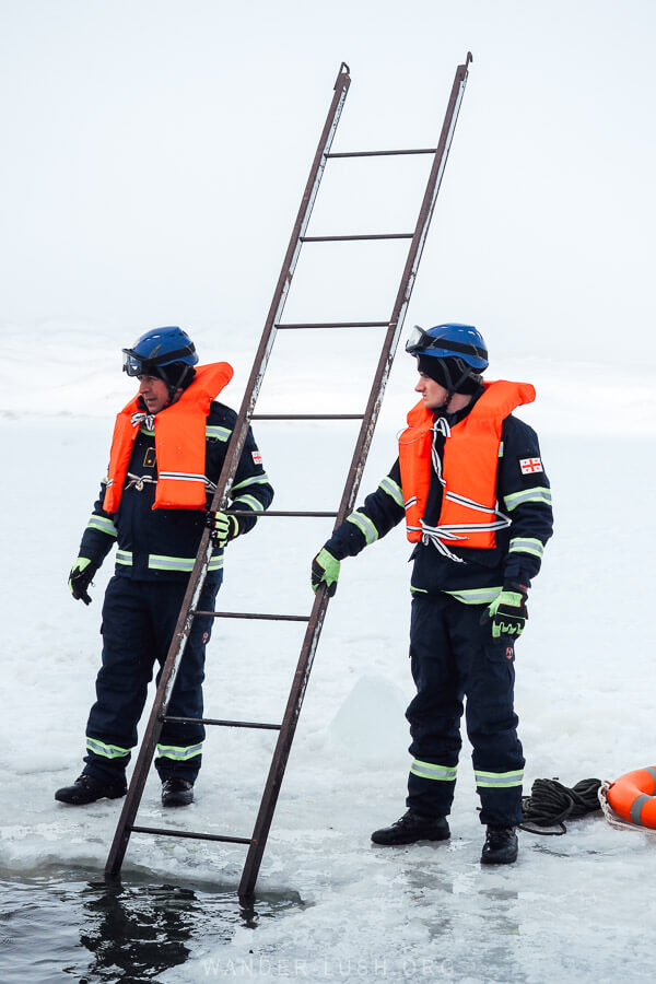 Two emergency service workers hold a ladder submerged in the frozen Paravani Lake in Georgia.