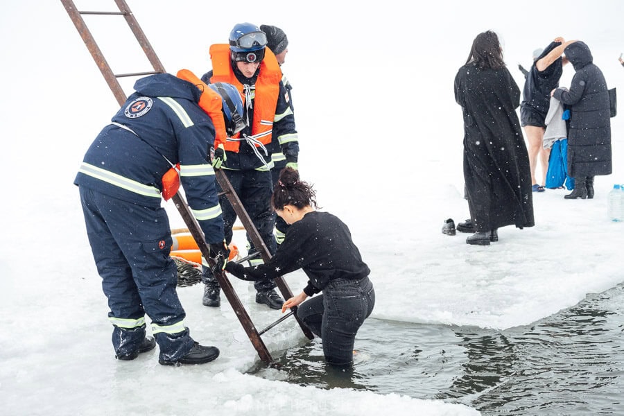 A woman dressed in black jeans and a sweater steps down a ladder into the freezing water of a lake on Epiphany Day in Georgia.