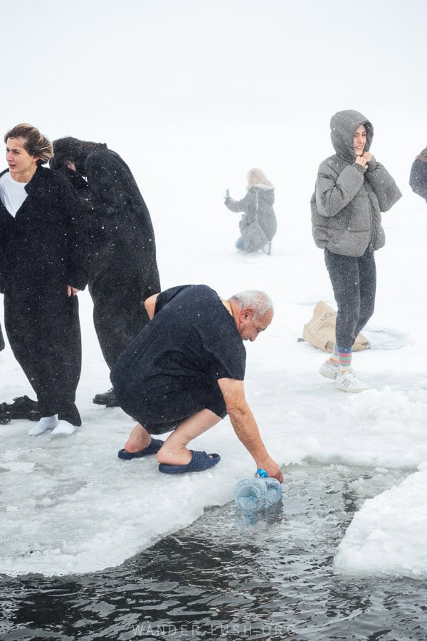 A man kneels on the edge of a hole in the ice to fill a bottle with lake water at Lake Paravani in Georgia.