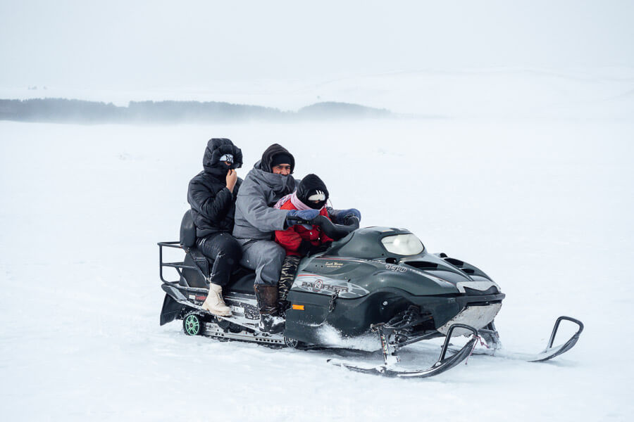 Three people ride a snow mobile across the frozen surface of a lake in Samtskhe-Javakheti, Georgia.