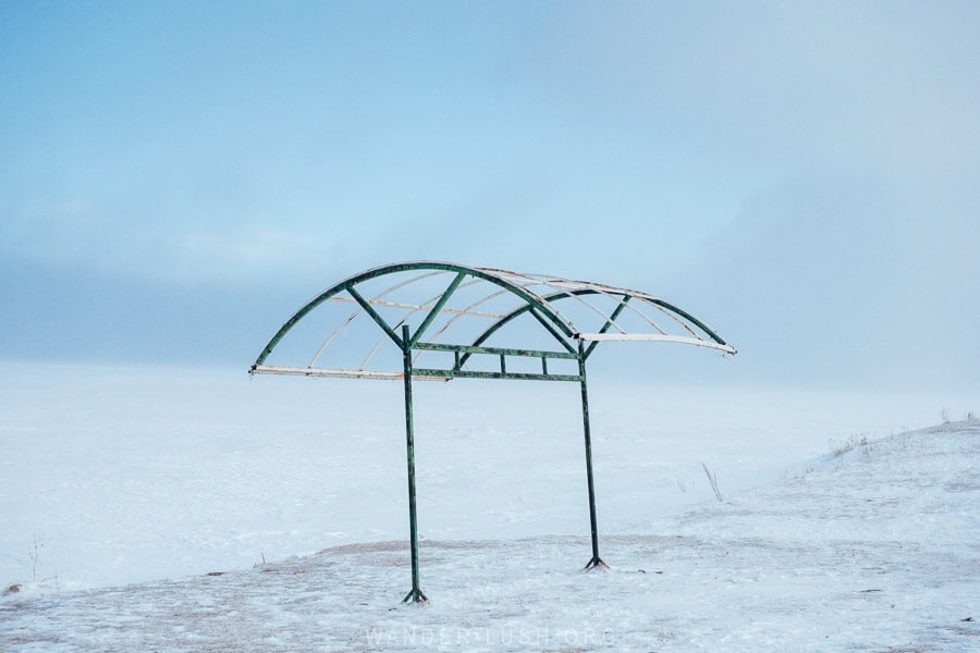 A destroyed metal shelter on the edge of Paravani Lake in winter, with snow all around.