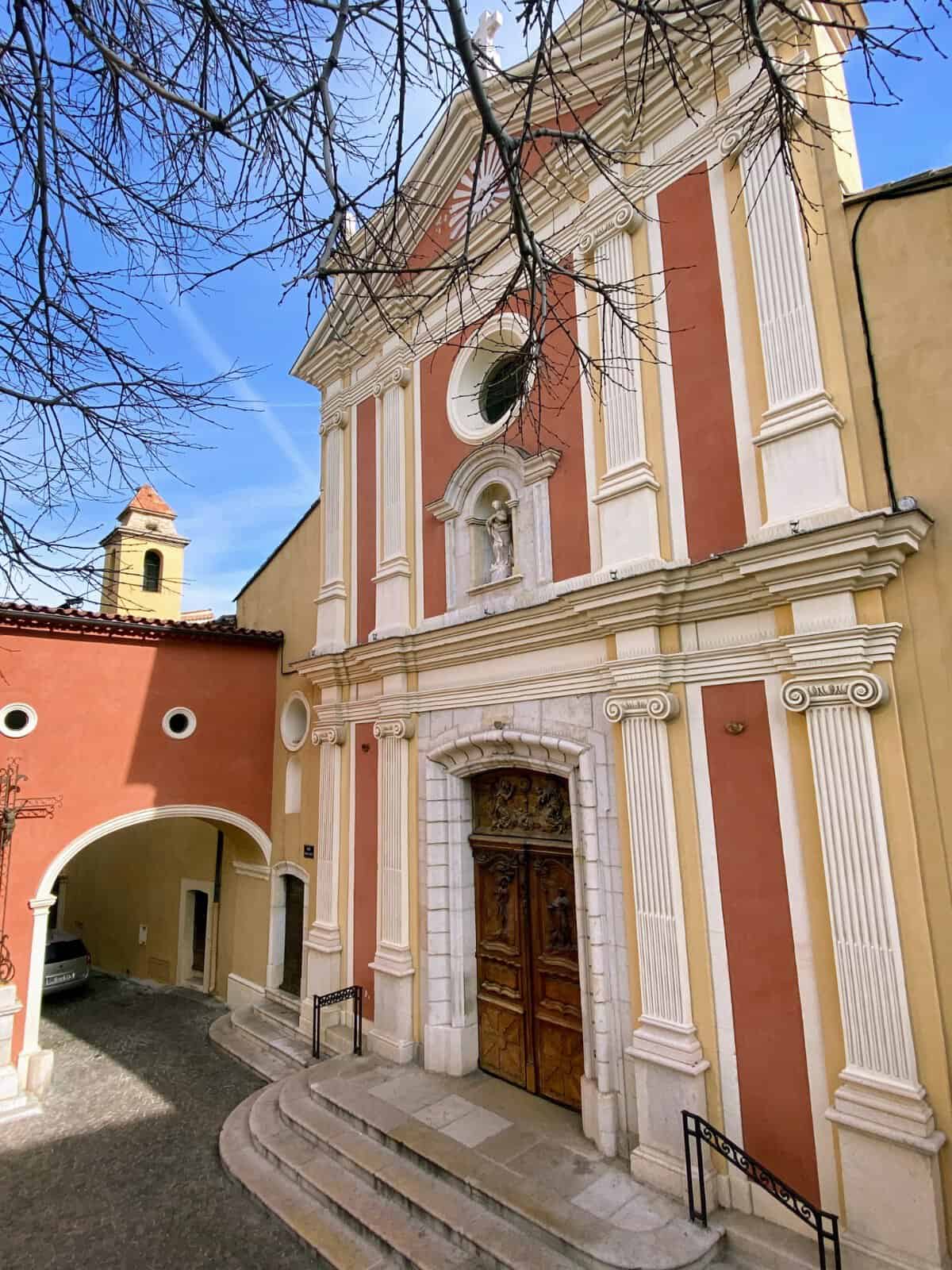 Outside of the Antibes Cathedral with pink exterior and wooden doors