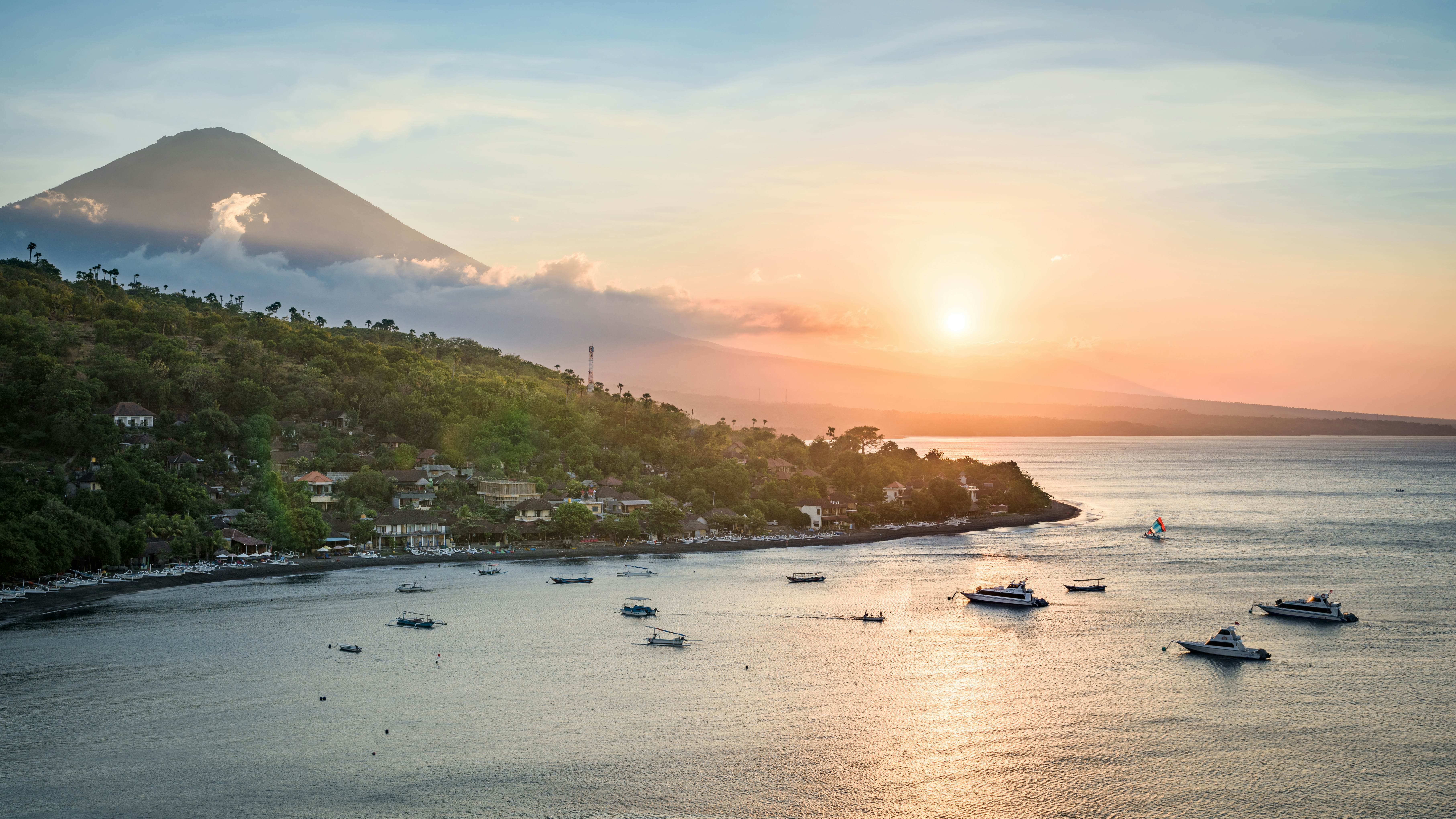 Sunset near a pointed coastal mountain with many small boats docked in a bay