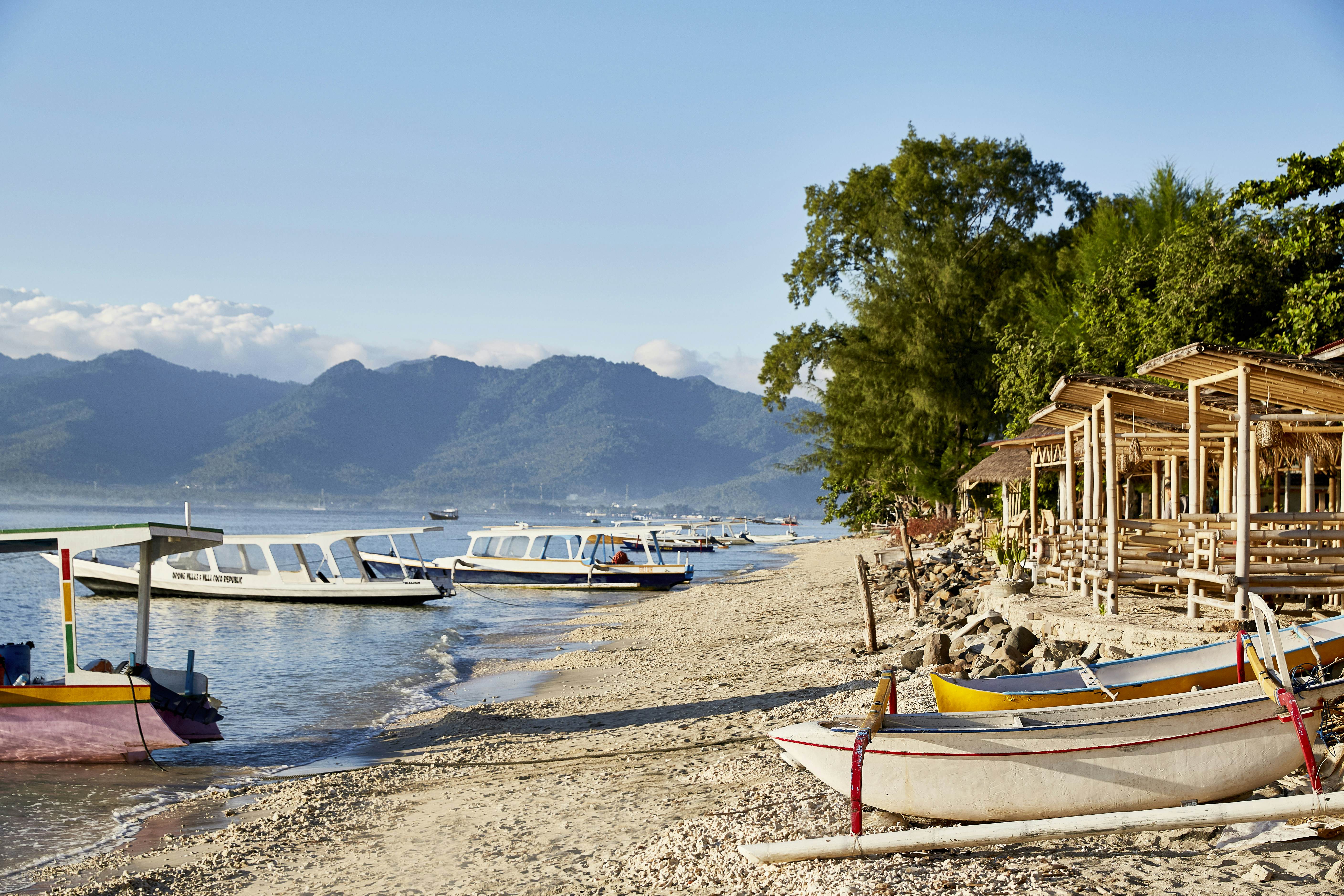 Small boats docked on a sandy beach lined with wooden shelters