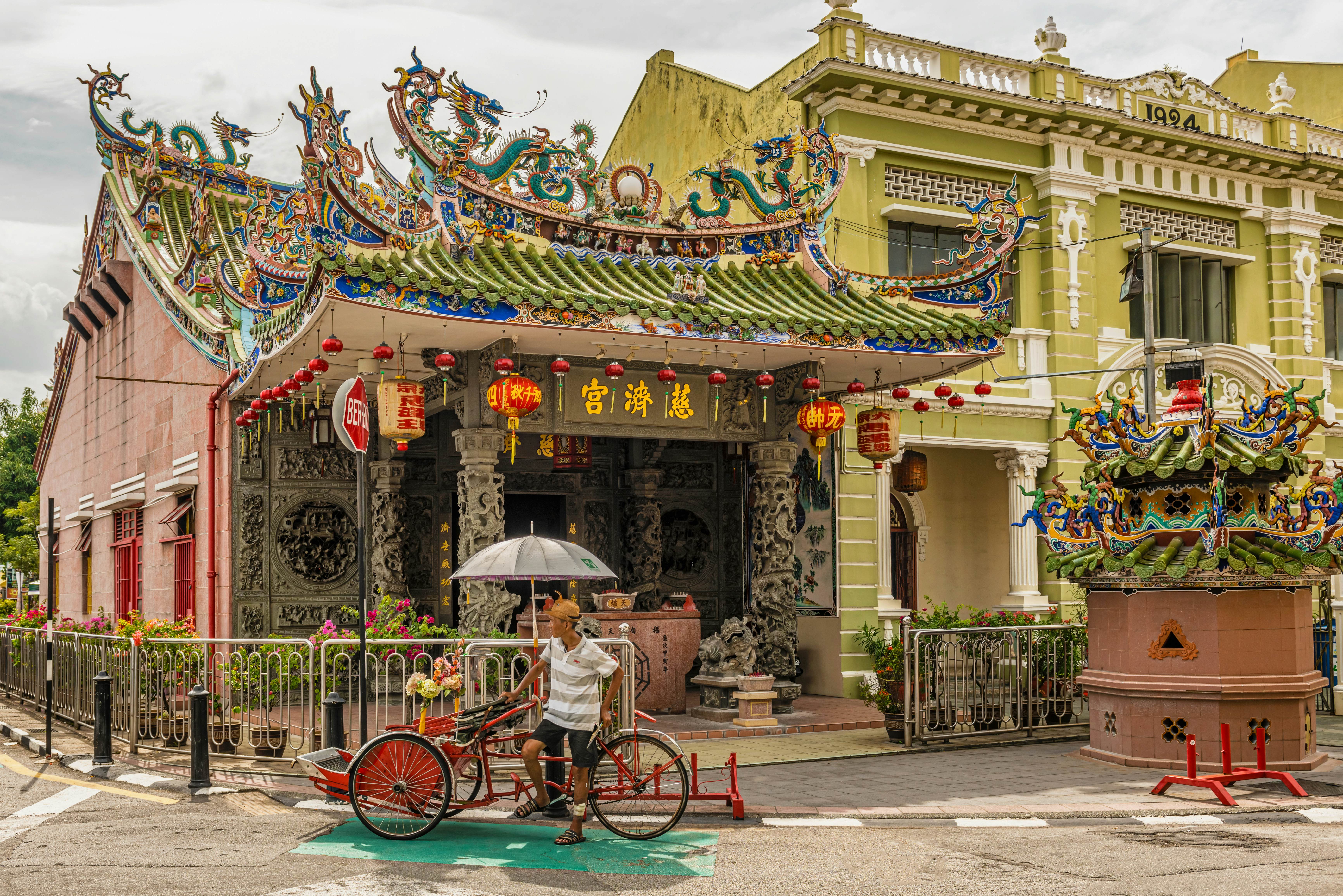 A man stands by a rickshaw outside a temple with Chinese-style red lanterns