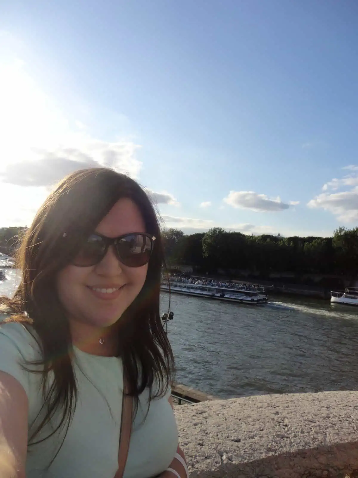 Riana wearing sunglasses and taking a selfie on a bridge over the River Seine in Paris